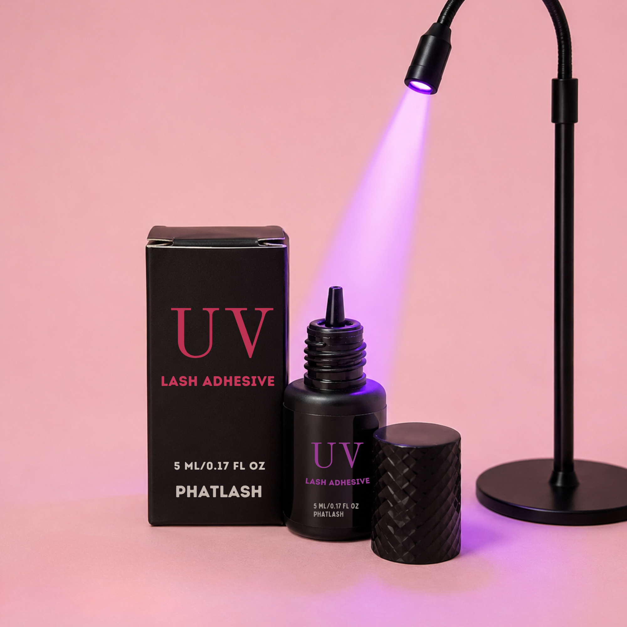 Phatlash UV Lash Adhesive bottle with its black box and cap, shown next to a black adjustable lamp emitting a purple UV light, on a pink background.